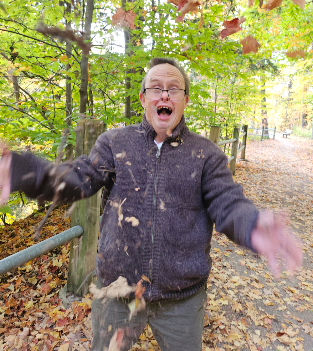 Man walking on trail in autumn, throwing leaves in air