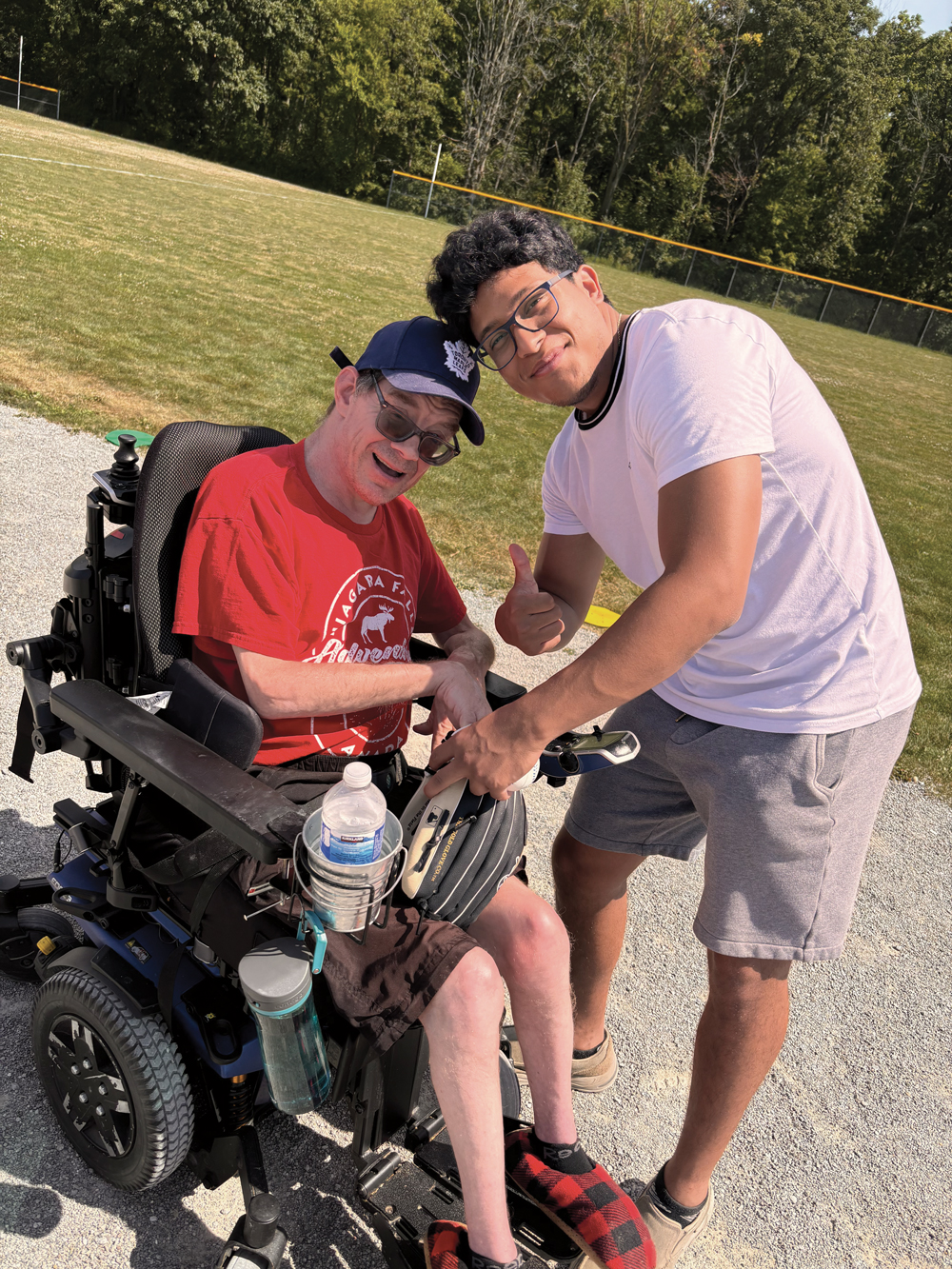 Two men on baseball field - one in wheelchair with glove - thumbs up